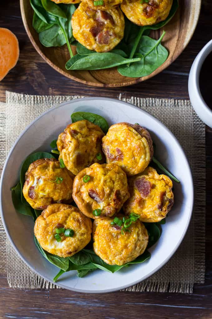 seven egg muffins on a bed of greens in a white bowl