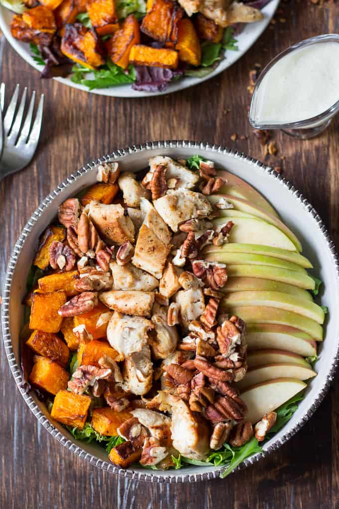 salad with butternut squash, sliced apple, pecans, and chicken in a bowl