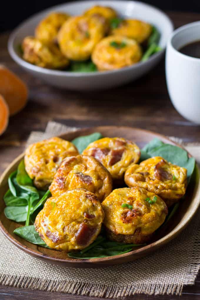 six bacon egg muffins on a bed of spinach in a wooden bowl