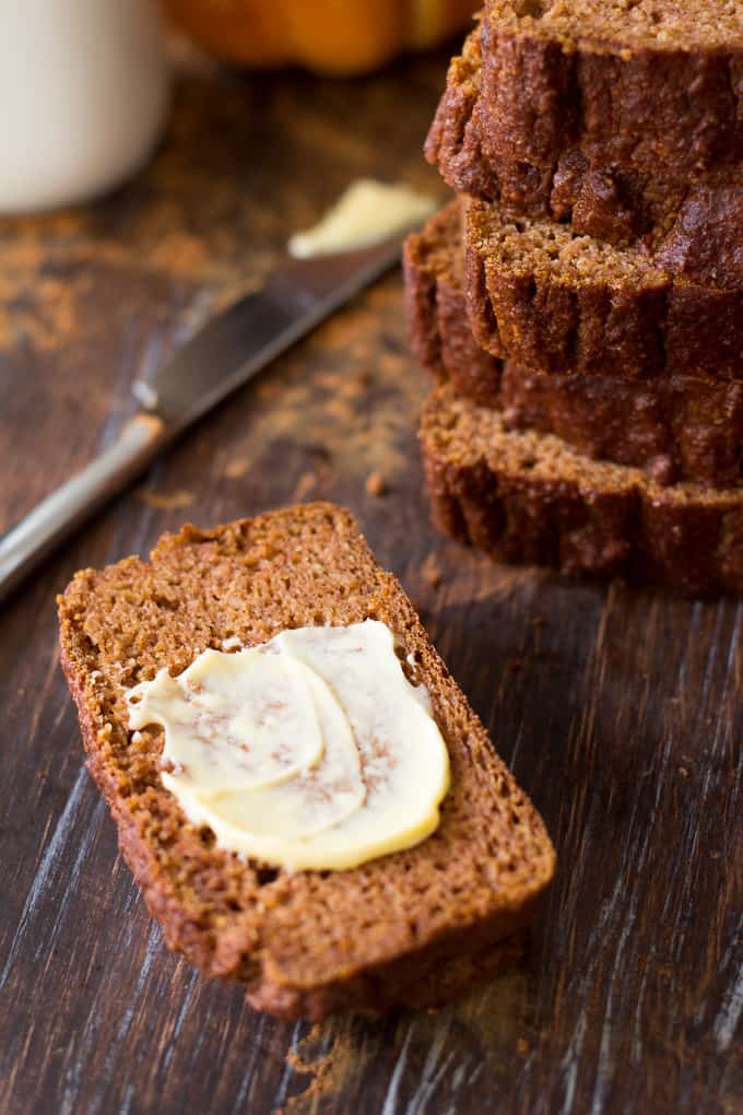 a slice of pumpkin bread with butter beside a stack of pumpkin bread slices