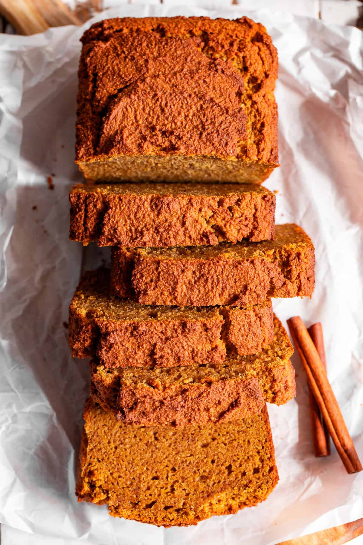 Sliced almond flour pumpkin bread on parchment paper with cinnamon sticks