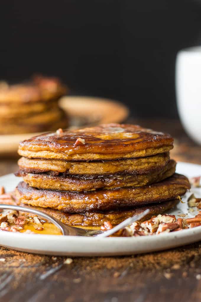 a stack of five paleo pumpkin pancakes on a white plate with chopped pecans for garnish