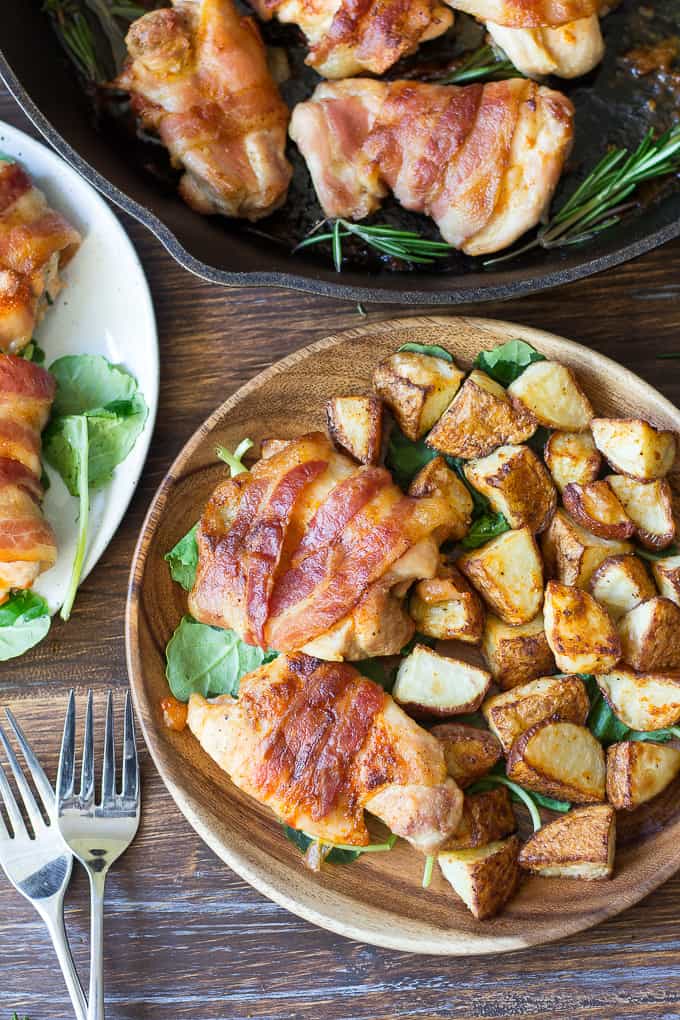 bacon wrapped chicken and crispy diced potatoes over spinach on a wooden plate