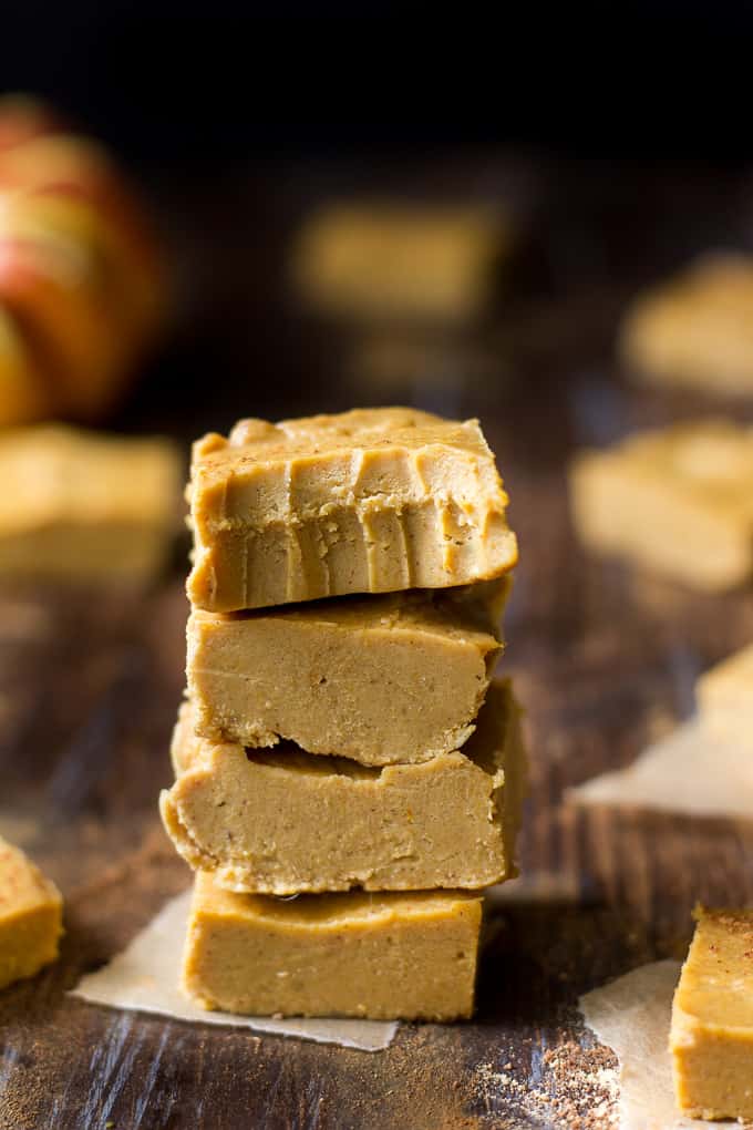 a stack of four squares of tan colored fudge on a board with scattered fudge squares in the background