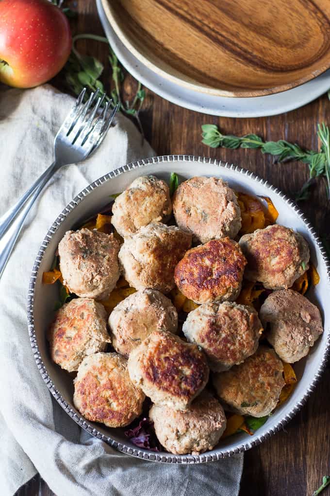 a large serving bowl of meatballs over salad on a wooden board