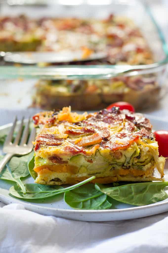 breakfast casserole on a plate of spinach with grape tomatoes on the side