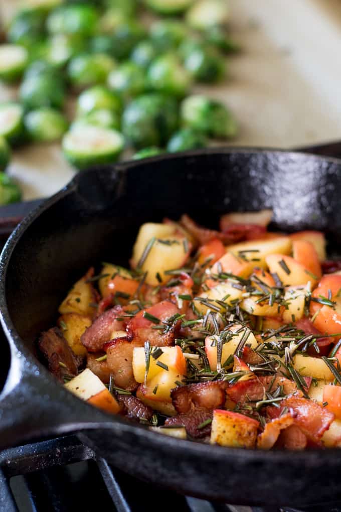 chunks of apples and bacon in a black skillet covered with chopped rosemary 