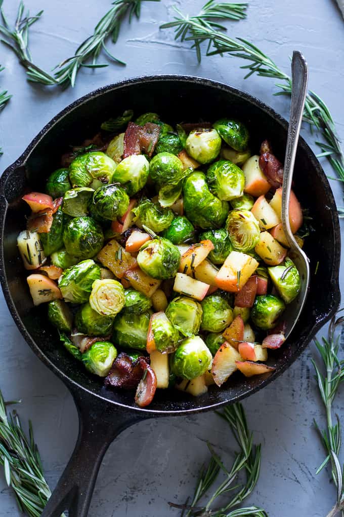 bright green brussels sprouts with apple chunks and bacon pieces in a black skillet