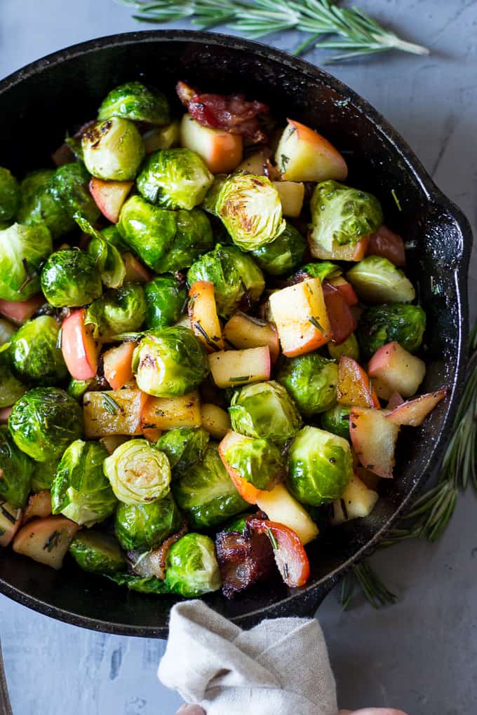 green cooked Brussels sprouts with bacon pieces and apple chunks in a black skillet