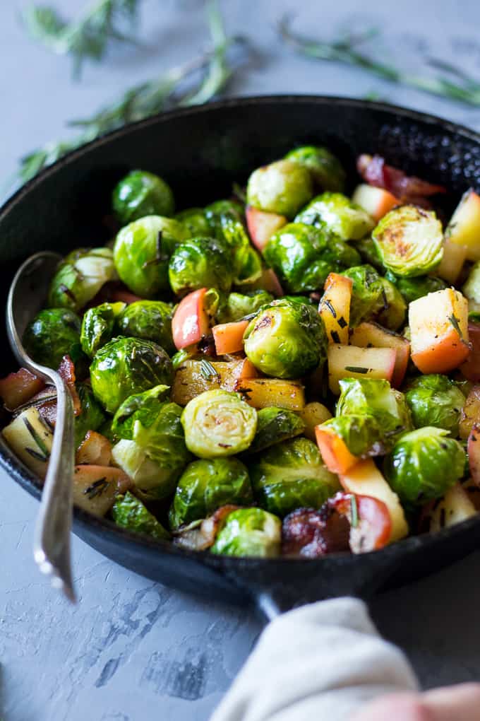 Brussels sprouts with apple and bacon pieces in a black skillet with a spoon