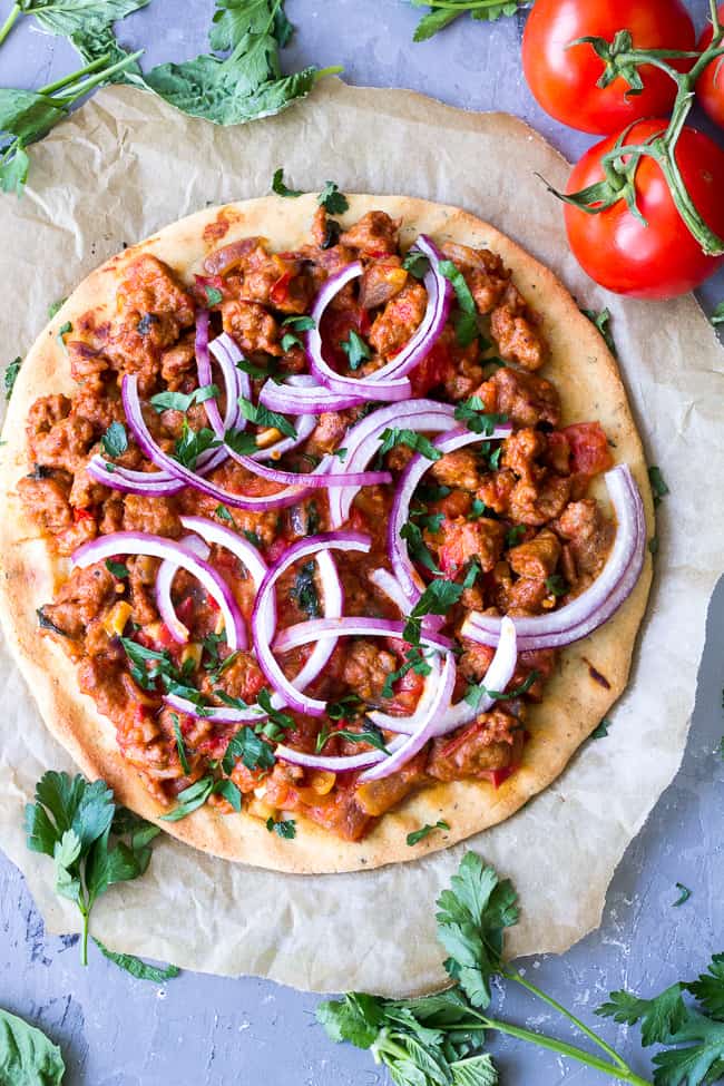 This hearty Paleo pizza has a thin, crisp and chewy crust with a sausage and fresh tomato basil topping that you can make spicy or mild to suit your tastes. The perfect filling and healthy pizza to make when a craving hits! Perfect 30 minute dinner for pizza night! Gluten free, dairy free, grain free, Paleo.