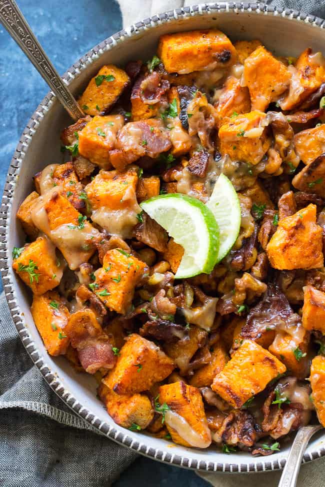 a bowl of sweet potato salad with bacon and walnuts garnished with two lime slices