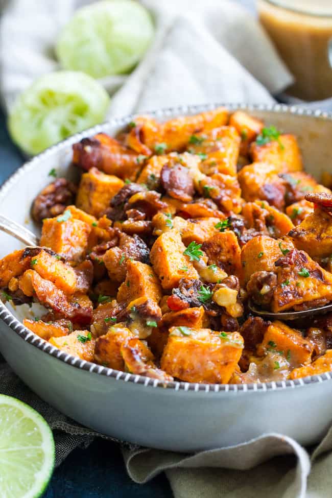 bowl of sweet potato salad in the forefront with limes and vinaigrette dressing in the background