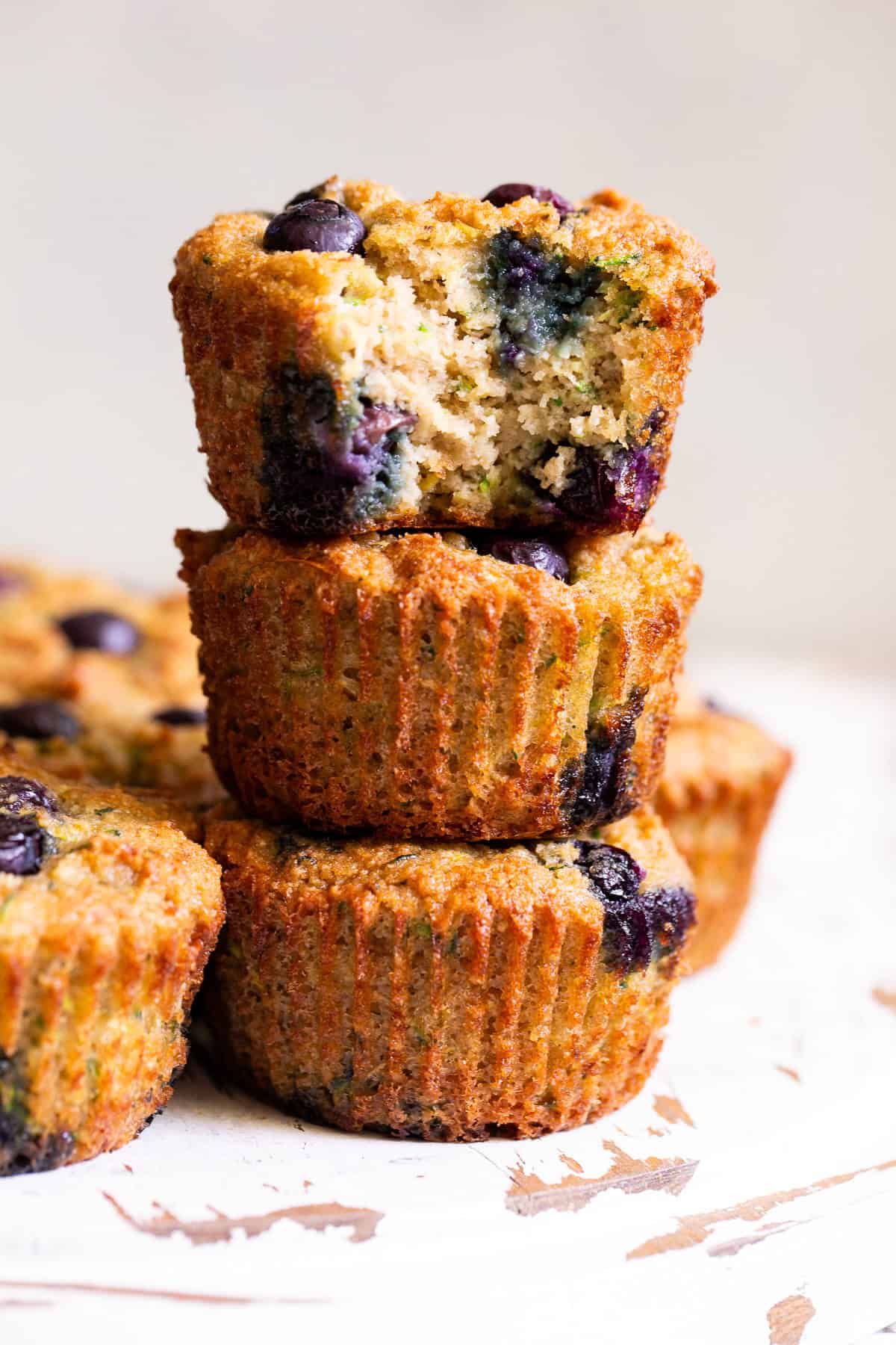 Gluten free blueberry zucchini muffins stacked on a white surface.