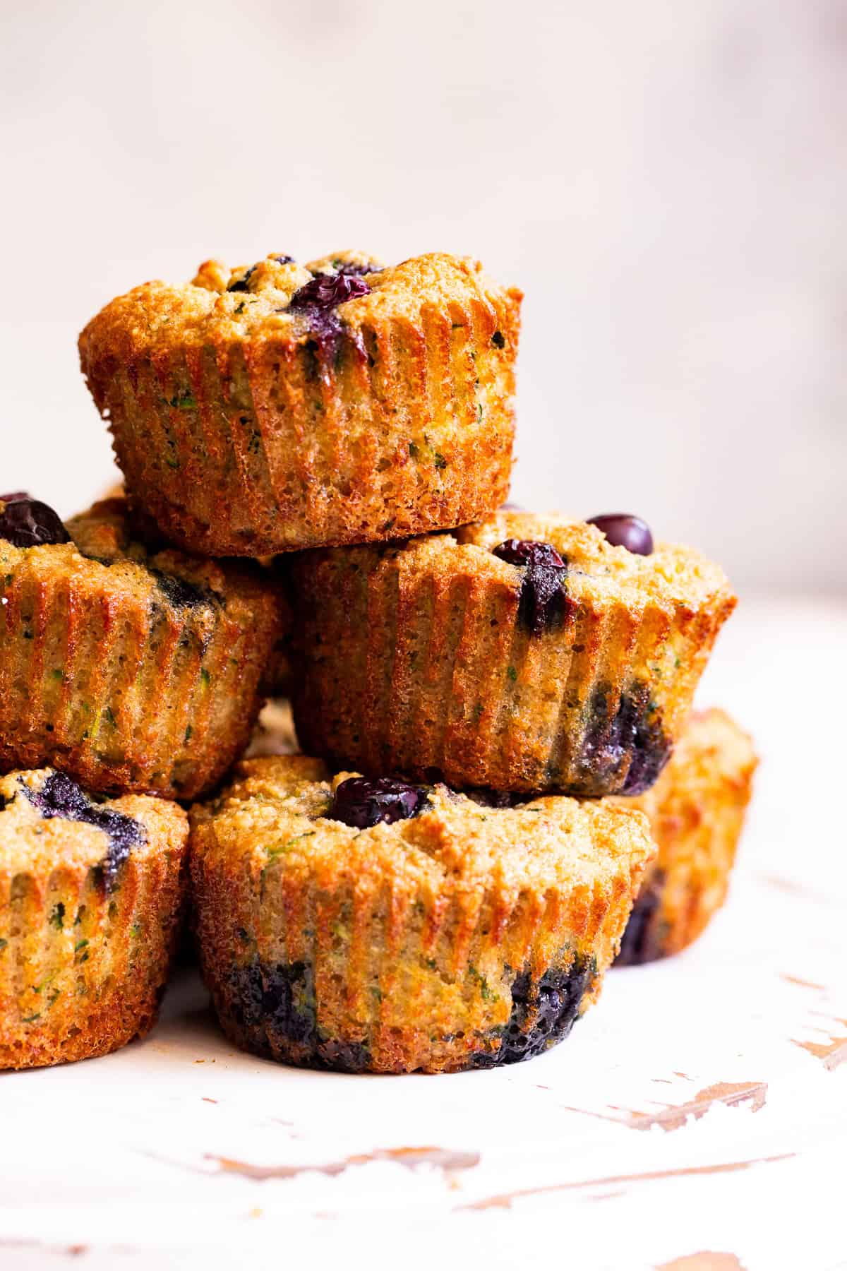 Gluten free blueberry zucchini muffins stacked on a white surface.