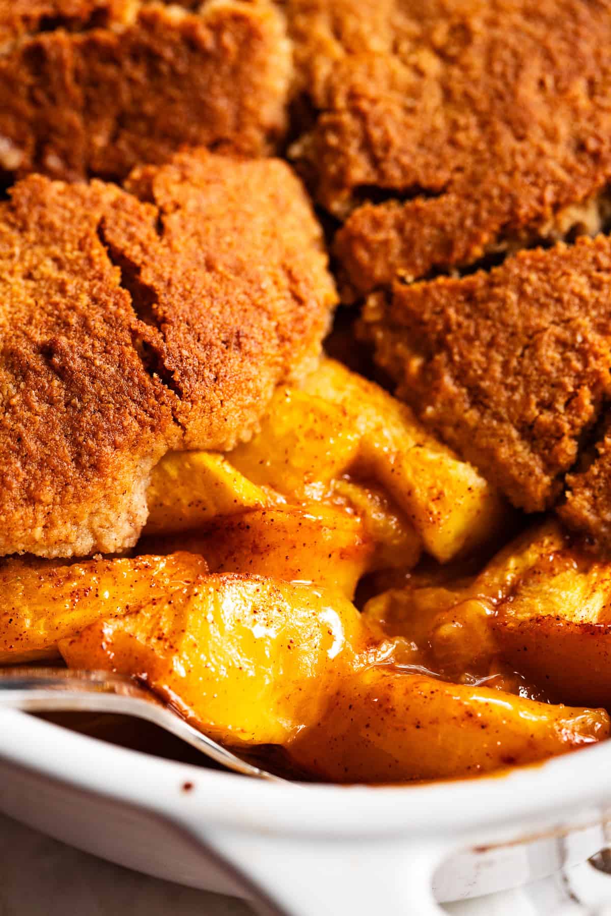 close up of easy peach cobbler in a baking dish with juicy peach filling