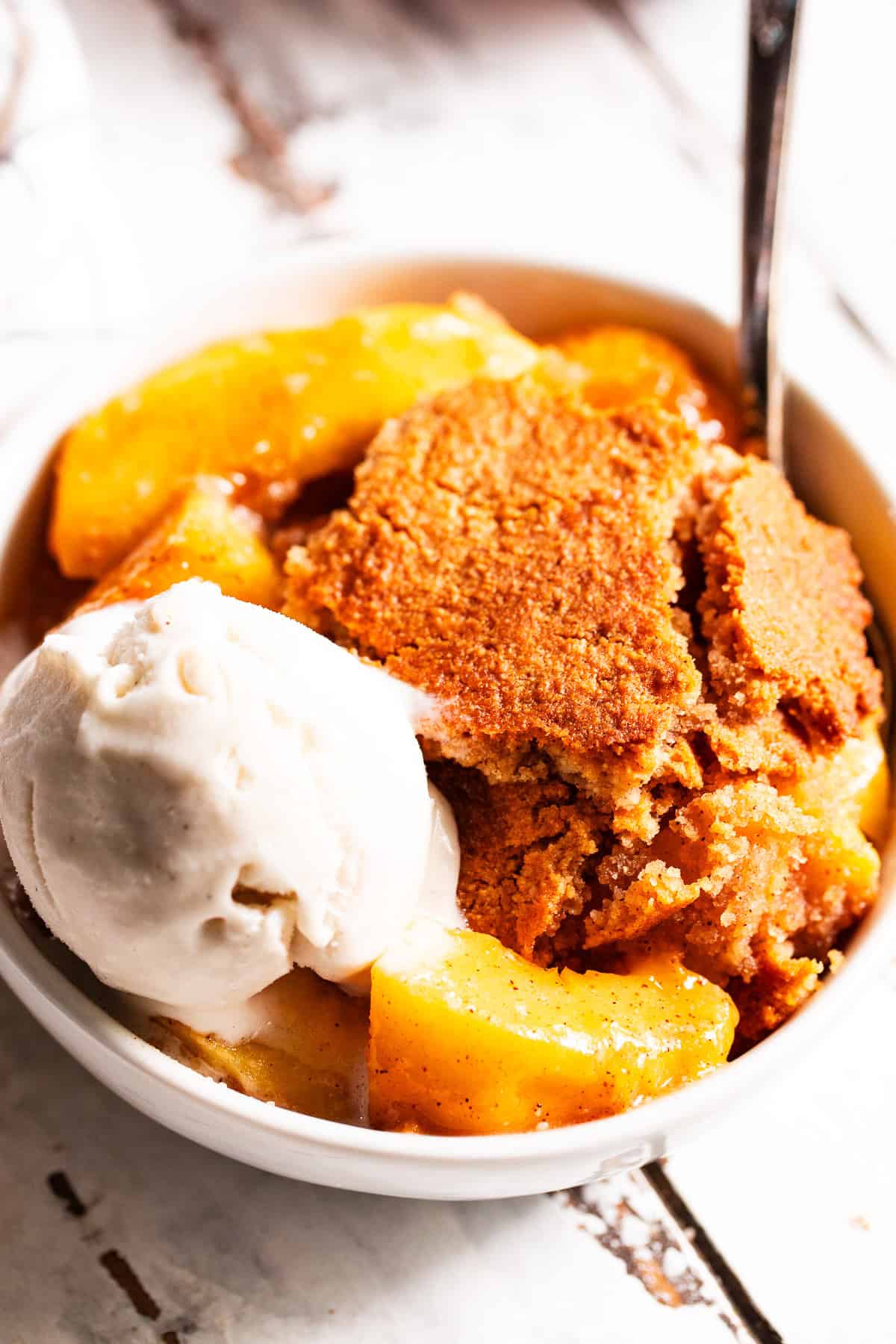 easy peach cobbler in a bowl with melting ice cream