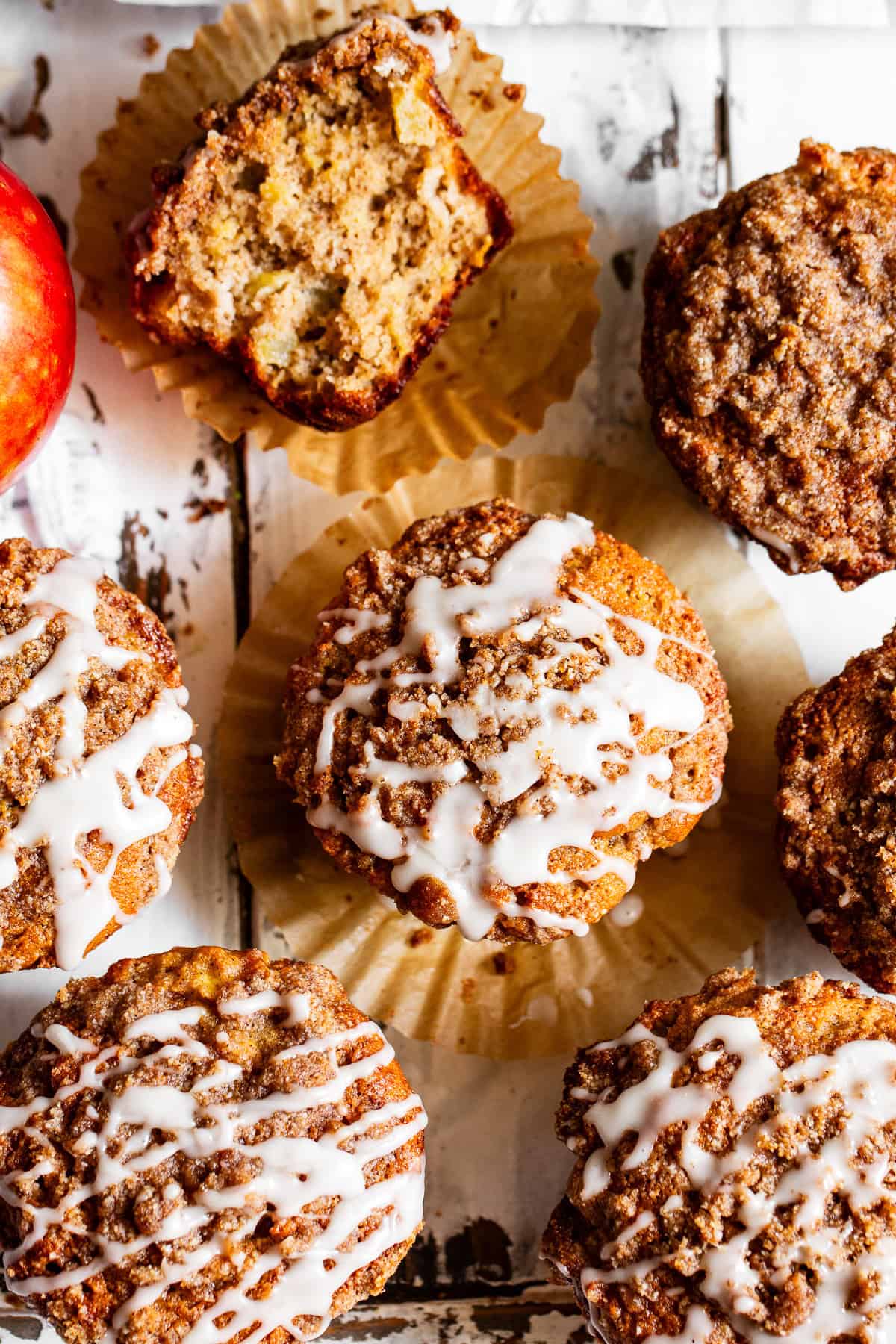 Overhead view of apple crumb muffins with cinnamon crumble, vanilla glaze, and one muffin broken open.