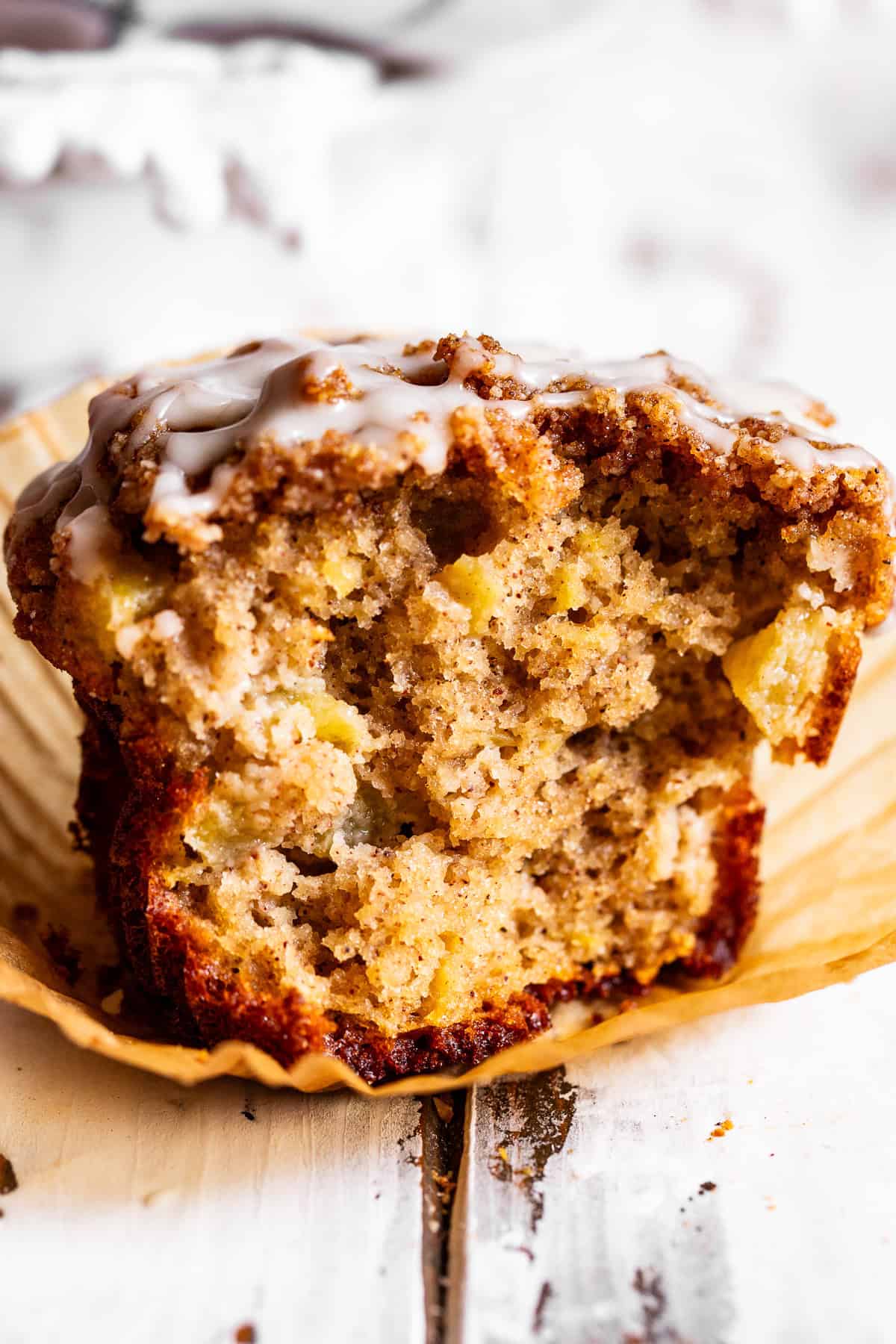 Apple crumb muffins with cinnamon crumb topping and a light vanilla glaze, with one muffin broken open to show the apple-filled center.