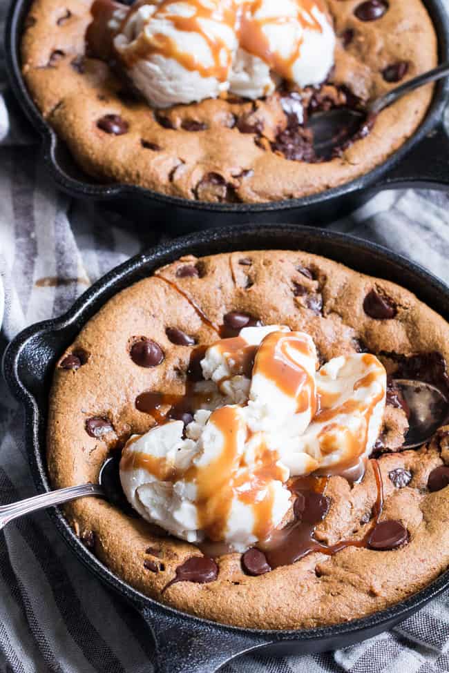two chocolate chip cookie skillets with scoops of white ice cream and caramel drizzle