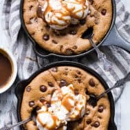 two brown chocolate chip cookie skillets with scoops of white ice cream and caramel drizzled on top