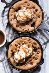 two brown chocolate chip cookie skillets with scoops of white ice cream and caramel drizzled on top