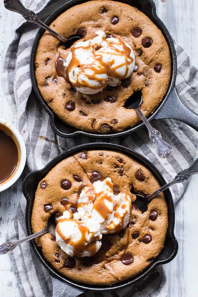 two brown chocolate chip cookie skillets with scoops of white ice cream and caramel drizzled on top