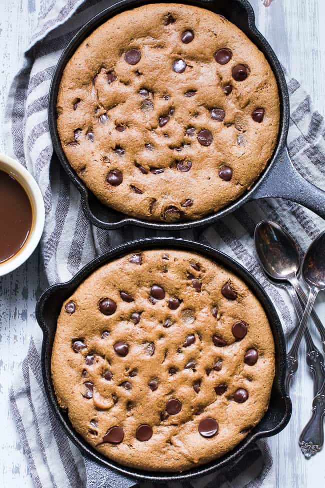 two cast iron skillets filled with baked cookie from edge to edge studded with chocolate chips