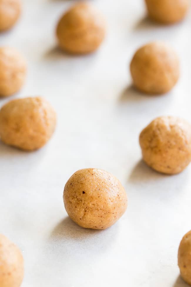 balls of tan colored cookie dough scattered on white parchment paper