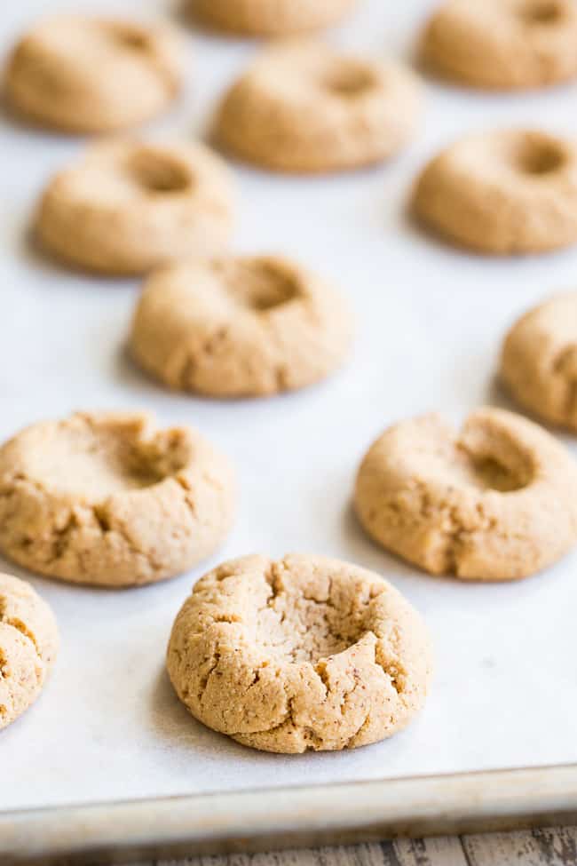 tan cookies with wells in the center scattered on a parchment paper lined baking sheet