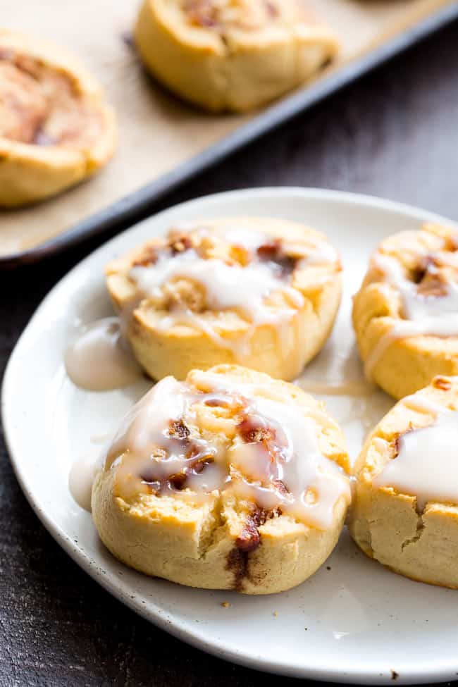 four cinnamon rolls drizzled with frosting on a white plate