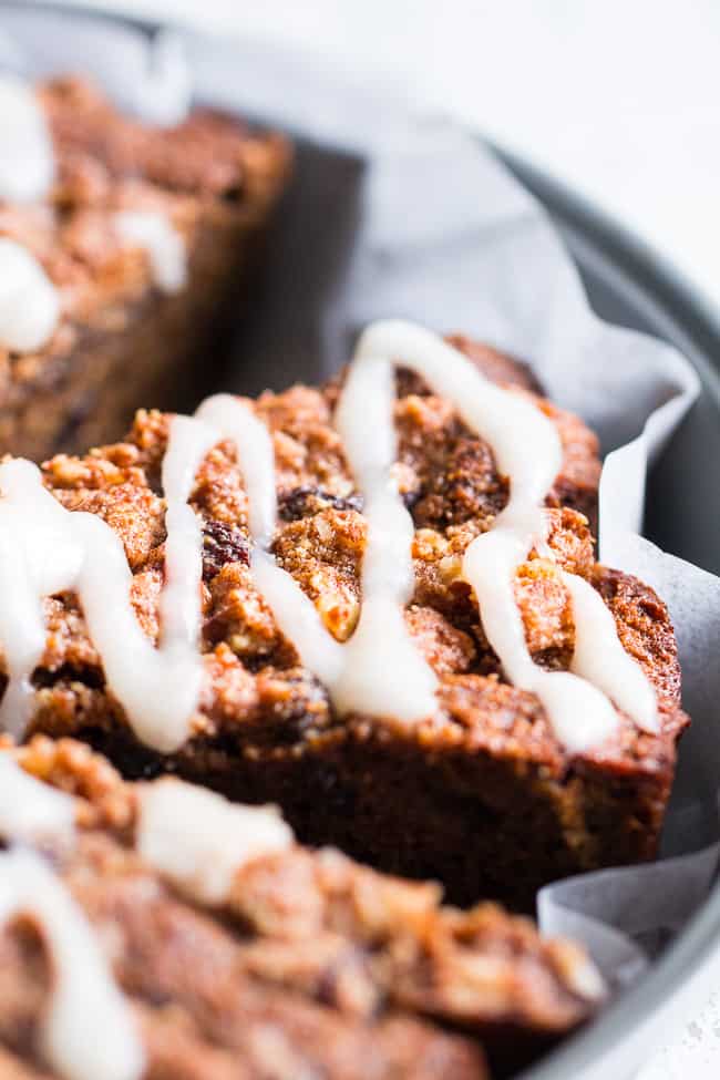 slices of a brown coffee cake drizzled with white frosting in a round gray cake pan lined with white paper 