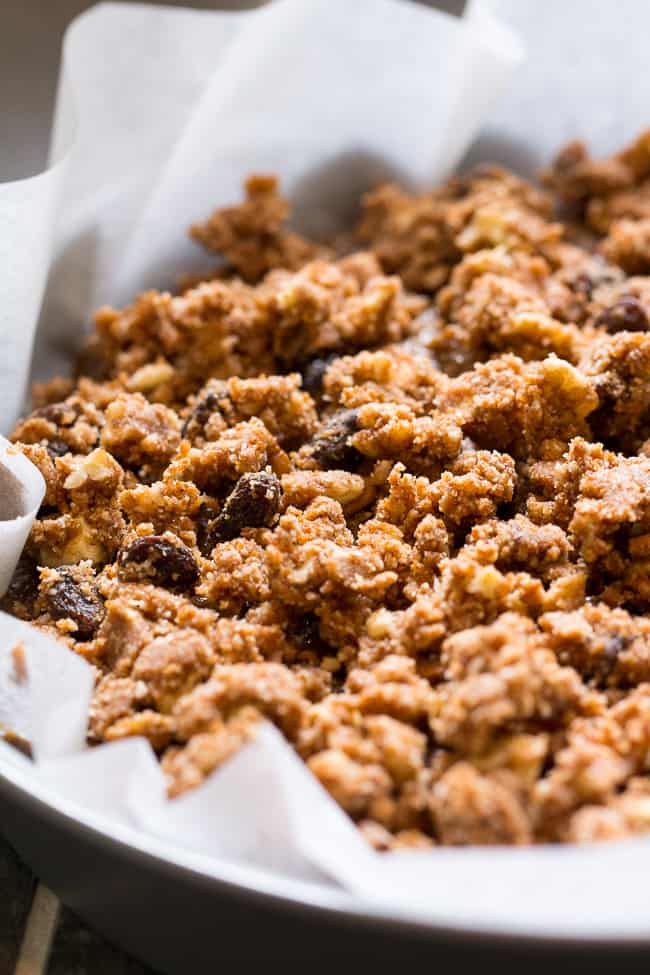 crumble topping with raisins and pecans on a cake in a round cake pan with parchment paper 