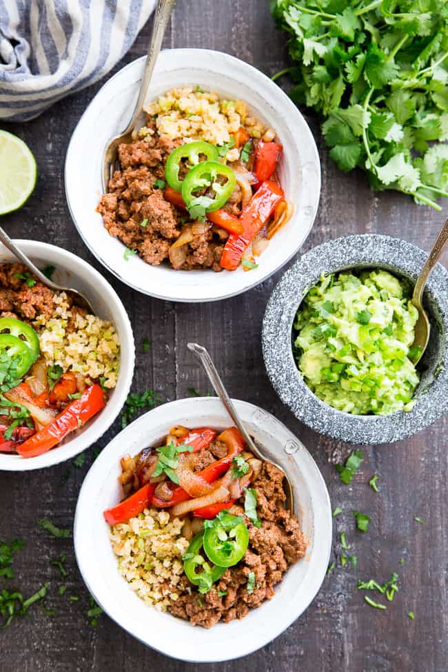 These easy, filling, totally satisfying Paleo Burrito Bowls are packed with spicy seasoned ground beef, sautéed peppers and onions, cauliflower rice and a quick guacamole.  Served over fried cauliflower rice with a kick for maximum flavor!   They're family approved, Whole30 compliant and keto friendly too!