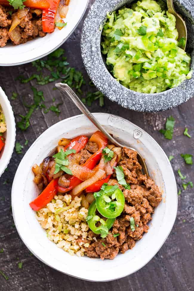 These easy, filling, totally satisfying Paleo Burrito Bowls are packed with spicy seasoned ground beef, sautéed peppers and onions, cauliflower rice and a quick guacamole.  Served over fried cauliflower rice with a kick for maximum flavor!   They're family approved, Whole30 compliant and keto friendly too!