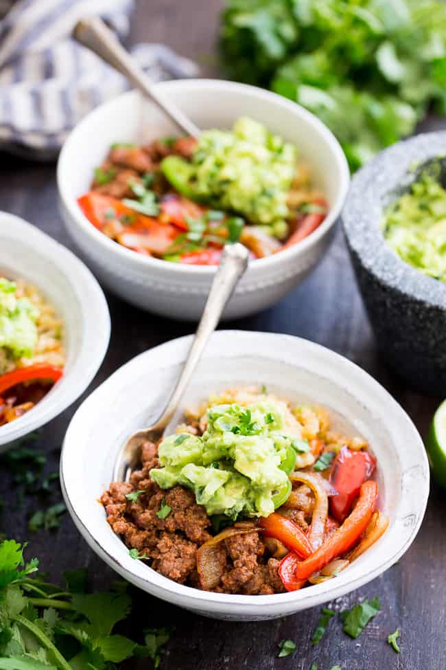 These easy, filling, totally satisfying Paleo Burrito Bowls are packed with spicy seasoned ground beef, sautéed peppers and onions, cauliflower rice and a quick guacamole.  Served over fried cauliflower rice with a kick for maximum flavor!   They're family approved, Whole30 compliant and keto friendly too!