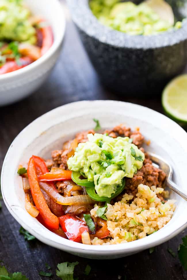 These easy, filling, totally satisfying Paleo Burrito Bowls are packed with spicy seasoned ground beef, sautéed peppers and onions, cauliflower rice and a quick guacamole.  Served over fried cauliflower rice with a kick for maximum flavor!   They're family approved, Whole30 compliant and keto friendly too!