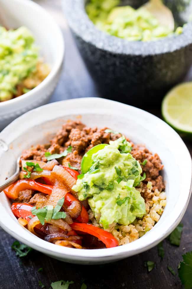 These easy, filling, totally satisfying Paleo Burrito Bowls are packed with spicy seasoned ground beef, sautéed peppers and onions, cauliflower rice and a quick guacamole.  Served over fried cauliflower rice with a kick for maximum flavor!   They're family approved, Whole30 compliant and keto friendly too!