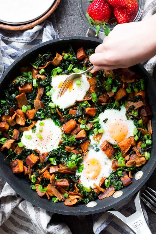 This simple sweet potato hash with kale and bacon is your new paleo and Whole30 go-to breakfast!  Crispy bacon, kale, and sweet potatoes are seasoned and cooked up perfectly in a big skillet, then topped with eggs and garnished with green onion.  It doesn't get easier or more delicious than this hash!  