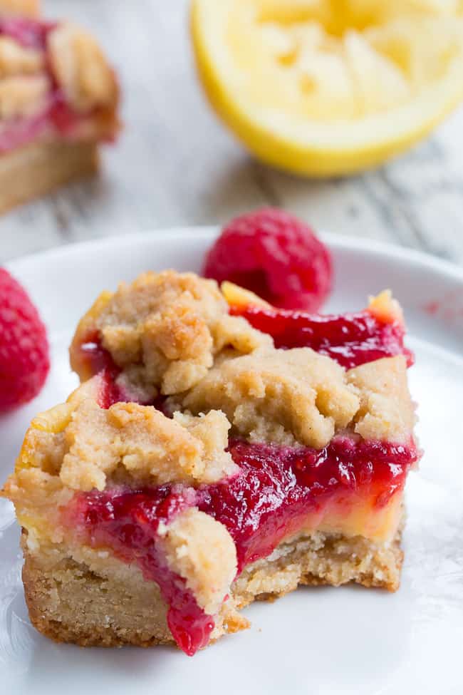 These paleo raspberry lemon bars are absolutely heaven!   A lemon cookie crust is topped with creamy tart sweet lemon curd, homemade raspberry sauce and more cookie crumbles to top.  Everything is baked to perfection and cut into bars for the ultimate dessert!  Gluten-free, dairy-free, no refined sugar, grain free.