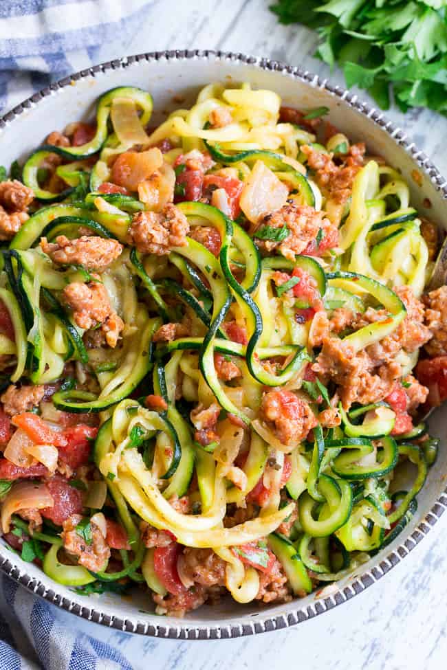 These zucchini noodles are made deliciously savory with lots of spicy Italian sausage, and a creamy tomato sauce.  Quick to throw together on a weeknight and easy to make ahead of time too!  It's a filling, family friendly lunch or dinner that's Paleo, Whole30, dairy free and low carb too!