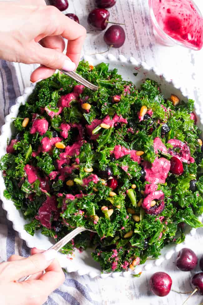 This paleo and vegan kale salad is packed with fresh cherries, blueberries, toasted pine nuts and almonds.  It's topped with a simple Whole30 compliant dressing made with fresh berries and cherries too!  Perfect as a side salad for summer or top it with your favorite protein for a full meal.  