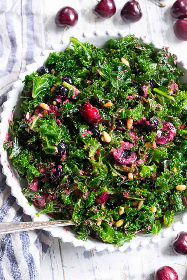 This paleo and vegan kale salad is packed with fresh cherries, blueberries, toasted pine nuts and almonds.  It's topped with a simple Whole30 compliant dressing made with fresh berries and cherries too!  Perfect as a side salad for summer or top it with your favorite protein for a full meal.  