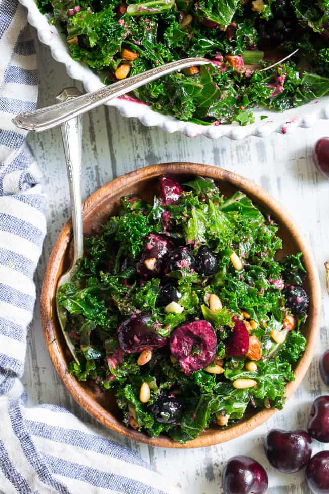 This paleo and vegan kale salad is packed with fresh cherries, blueberries, toasted pine nuts and almonds.  It's topped with a simple Whole30 compliant dressing made with fresh berries and cherries too!  Perfect as a side salad for summer or top it with your favorite protein for a full meal.  