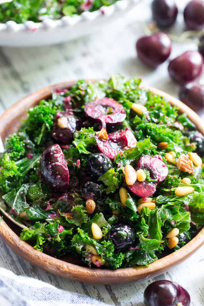 This paleo and vegan kale salad is packed with fresh cherries, blueberries, toasted pine nuts and almonds.  It's topped with a simple Whole30 compliant dressing made with fresh berries and cherries too!  Perfect as a side salad for summer or top it with your favorite protein for a full meal.  