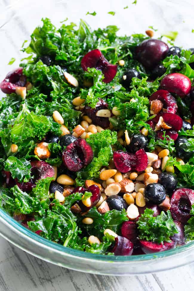 This paleo and vegan kale salad is packed with fresh cherries, blueberries, toasted pine nuts and almonds.  It's topped with a simple Whole30 compliant dressing made with fresh berries and cherries too!  Perfect as a side salad for summer or top it with your favorite protein for a full meal.  