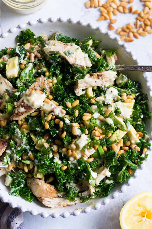 This Paleo and Whole30 Kale Chicken Caesar Salad is an easy, healthy lunch or dinner packed with so much flavor!  Grilled chicken is tossed with avocado, toasted pine nuts, chopped kale, and a creamy homemade dairy-free caesar dressing for a deliciously savory salad that you'll want to make again and again.