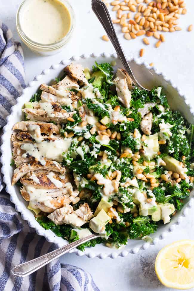This Paleo and Whole30 Kale Chicken Caesar Salad is an easy, healthy lunch or dinner packed with so much flavor!  Grilled chicken is tossed with avocado, toasted pine nuts, chopped kale, and a creamy homemade dairy-free caesar dressing for a deliciously savory salad that you'll want to make again and again.