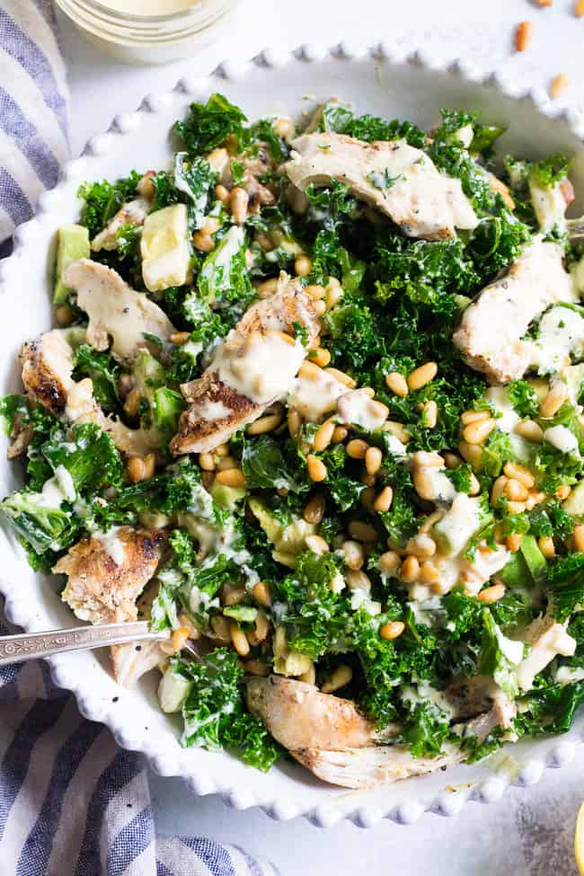 This Paleo and Whole30 Kale Chicken Caesar Salad is an easy, healthy lunch or dinner packed with so much flavor!  Grilled chicken is tossed with avocado, toasted pine nuts, chopped kale, and a creamy homemade dairy-free caesar dressing for a deliciously savory salad that you'll want to make again and again.