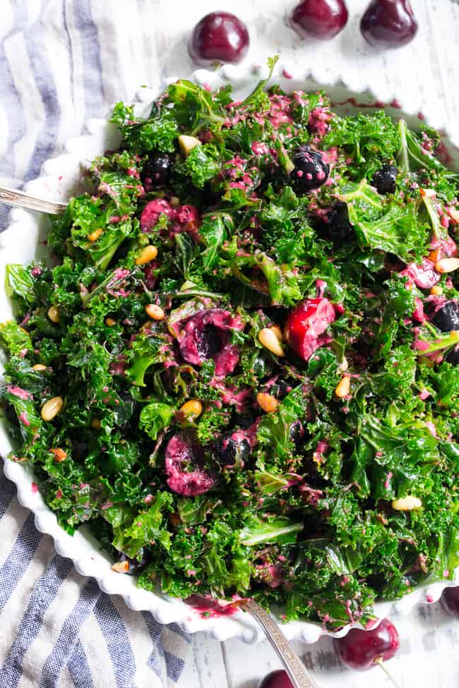 This paleo and vegan kale salad is packed with fresh cherries, blueberries, toasted pine nuts and almonds.  It's topped with a simple Whole30 compliant dressing made with fresh berries and cherries too!  Perfect as a side salad for summer or top it with your favorite protein for a full meal.  